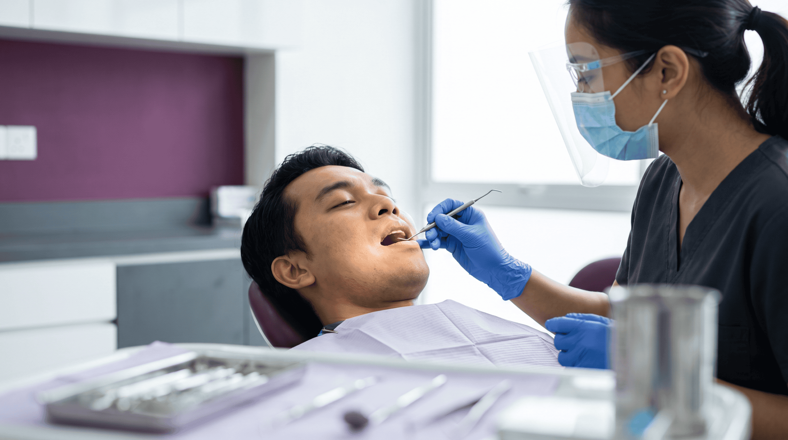 Dentist performing oral exam on patient in dental clinic setting.